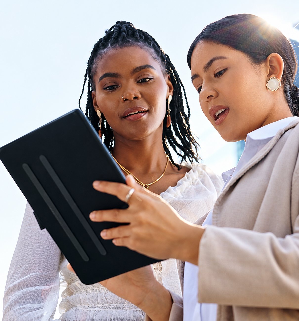 Deux jeunes femmes en tenue élégante consultent attentivement une tablette noire à la lumière du jour.